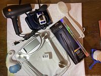 Lot contents overview on white cloth. Conair hair dryer, digital BP monitor with cuff, bathroom scale, hair straightener box, back scrub brush, and personal massager visible.