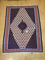 Full view of Persian wool carpet laid flat showing central white diamond medallion on navy blue background with floral motifs and multi-colored geometric borders.