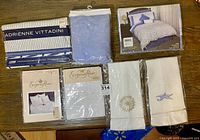 Photo showing a collection of new white cotton bedding and linens including fitted sheet, flat sheet, pillow shams, tea towels, some packaged