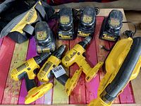 View of three used DeWalt 18V cordless drills, four battery chargers, and a DeWalt tool bag on a table.