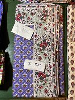 Folded floral tablecloth showing label and pattern on purple background with cream floral border.