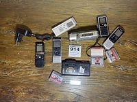 Photo showing 7 handheld tape recorders on wooden surface with several cassette tapes, power cord, and label with lot number 914