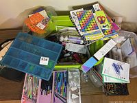 Wide view of crafting supplies on table showing pens, blue organizer, green bin, stencils, and boxed craft tools.