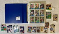 Blue binder holding the 1989 Topps NFL card set with clear plastic sleeves, surrounded by unopened and opened packs of football cards from various brands.