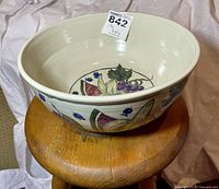 Ceramic bowl resting on a wooden stool with visible fruit motifs on inside and outside surfaces, showing size and shape.