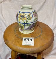 Full view of the vase on a wooden stool showing its size compared to a label with dimensions.