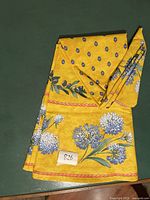 Folded view of yellow cotton tablecloth with blue and white floral prints and green leaves