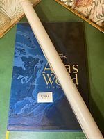 Rolled large plasticized wall map placed over the cover of the atlas book.