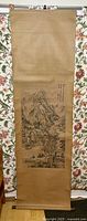 Full view of a vintage wall scroll hanging against floral background, showing scroll top and bottom rod, with mountain landscape artwork and calligraphy on fabric background
