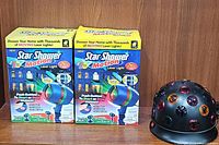 Two boxed Star Shower Motion laser lights and one vintage revolving carousel disco light on wooden surface
