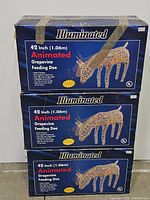 Three stacked boxes of 42 inch Animated Illuminated Grapevine Feeding Doe decorations, blue packaging with doe graphic and text detailing indoor/outdoor use, animation, and lighting.