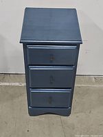 Front view of blue wooden nightstand showing all three drawers closed.