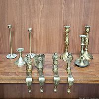 Photo showing 7 brass candlestick holders of different styles and sizes, plus 4 brass stocking holders with festive figures.