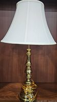 Full view of one brass lamp with white fabric shade on dark wood surface.