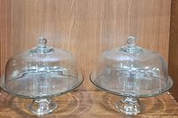 Pair of clear glass cake stands with dome covers, showing the overall look and matching design.