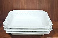 Stack of three white ceramic serving platters showing their shape and thickness, with etched pattern visible on edges.