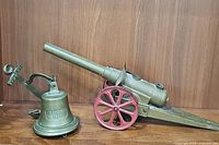 Vintage brass nautical ship bell with anchor bracket and Conestoga carbide cannon collectible displayed on wooden surface.