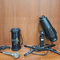 Photo showing all three items: outdoor projector on tripod, Corona wireless speaker, and microphone on table.