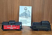 Pennsylvania Flyer red caboose and black coal tender train cars with Lionel owner's manual behind them on wooden surface.