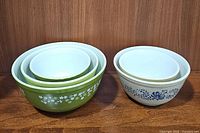 Set of 5 vintage Pyrex mixing bowls, 3 green Spring Blossom and 2 brown Homestead, stacked and displayed on wood surface