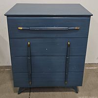 Front view of modern blue 4-drawer chest showing four drawers with gold tipped blue handles and minor surface wear.