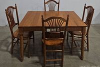 View of oak rectangular dining table with four matching wheat back chairs around it.