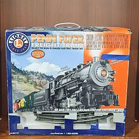 Front of the box showing the Penn Flyer Freight Train set with image of black steam locomotive and freight cars on mountainous background, including set size and features.