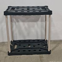 Front view of Rubbermaid plastic tool holder showing two black perforated shelves supported by four beige vertical legs.