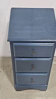 Front view of the blue nightstand showing all three drawer fronts closed, each with a metal knob.