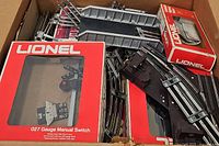 Box containing Lionel 027 gauge manual switch in original red box with curved tracks and other boxed Lionel accessories.