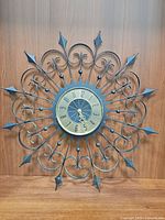 Metal starburst floral wall clock with ornamental metal frame and readable clock face showing the time 6:30.