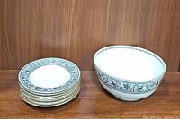Stack of eight soup/pasta bowls alongside the large serving bowl on a wooden shelf.