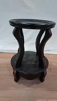 Front view of the black wooden stand showing curved legs and round base