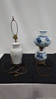 Pair of ceramic blue flowered lamps on black cloth background showing full lamp body and harp fittings.