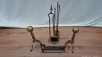 Full view of complete brass fireplace accessory set showing andirons and tool stand with tools.