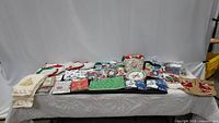 Large assortment of Christmas and winter-themed linens and decorations spread out on a table, showing multiple folded towels, pot holders, napkins, socks, and other festive items.
