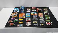 Overview of 34 collectible cars laid out on black cloth showing various brands and packaging types including boxed and bagged items
