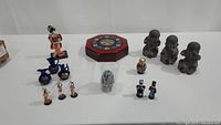 Photo showing grouped figurines including blue ceramic pitchers, small traditional dolls, octagonal box, and vintage style figures