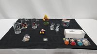 Wide view of all items arranged on a black cloth showing mugs, figurines, tin box and paint pots.