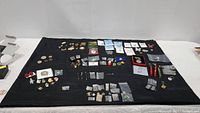 Wide layout of entire collection on black cloth showing arranged pins, brooches, coins, key rings, and medals.