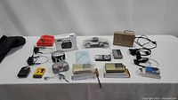 Wide image showing full lot of radios, headphones, and Walkman displayed on a table, including various models, cables, boxes, and the car radio model in wrap.