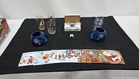 Seven glassware items with Redskins logos, two blue ceramic ashtrays, trading cards box, figurines, and holiday card strip on black cloth.