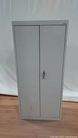 Front view of the light gray metal cabinet with double doors and visible minor marks.