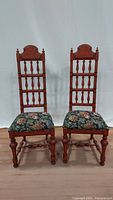 Two vintage Thomasville wooden chairs with vertical spindle backs and floral upholstered seats, standing side by side on a wooden floor against a white backdrop.