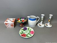 Five ceramic pieces displayed together including candlestick holders, square flower frog, floral comport, small majolica plate, and white pitcher.