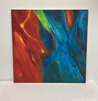 Front view of the abstract oil painting showing vibrant swirls of red, blue, and green colors on a square canvas.