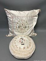 Image of the square pillow in light cream satin fabric featuring embroidered cranes with detailed floral and pine needle stitching.