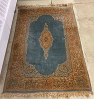 Top-down view of rectangular Chinese area rug with a blue center and orange floral patterned borders, showing fringed edges and signs of wear.