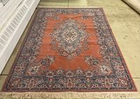 Full view of orange oriental rug with central medallion and fringed edges
