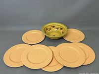 Grouped image showing one pottery bowl surrounded by eight peach-colored plates on gray background